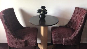 A room with a round table, two patterned chairs, a black and white tiger painting on the wall, and a vase with black flowers on the table. - Dunes Motel (Bend)