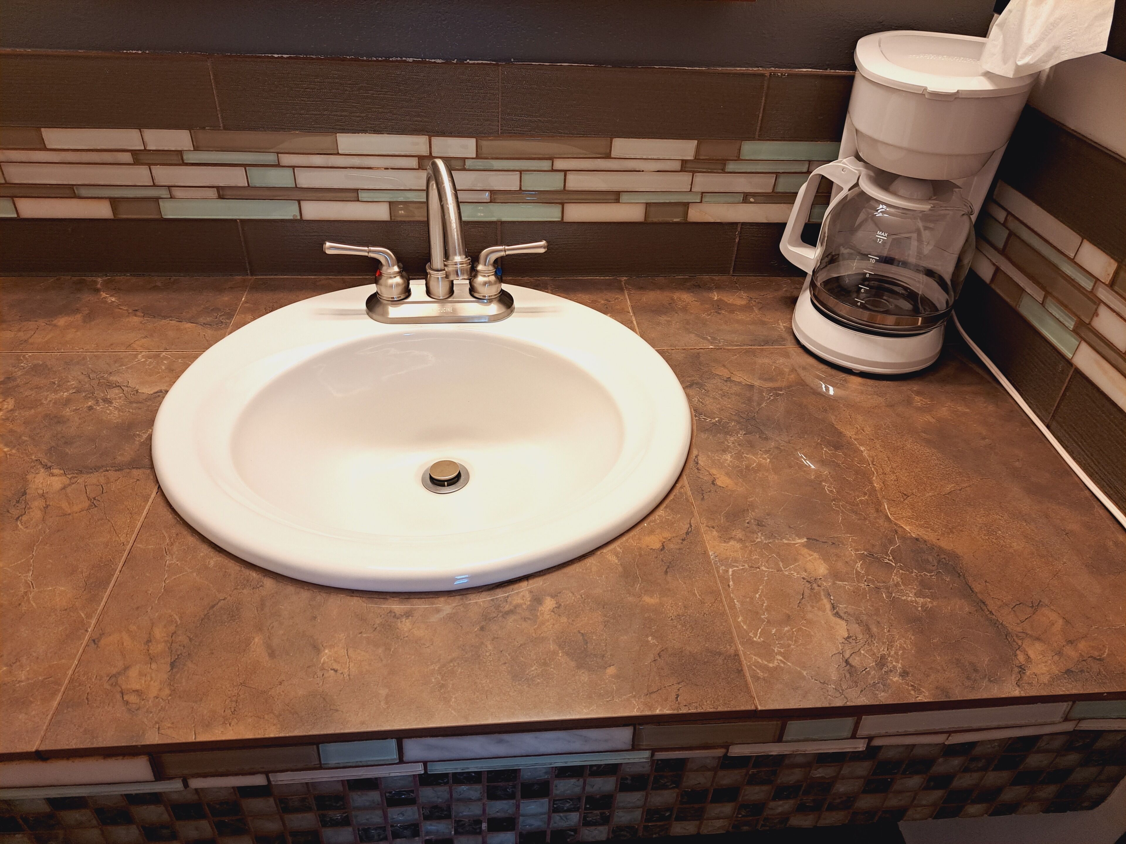 A bathroom sink with a modern faucet, a coffee maker, and a tiled backsplash.