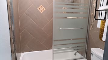 A modern bathroom with a glass shower enclosure, a white bathtub, and a toilet.