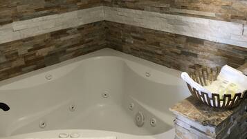 Un baño en esquina con pared de mosaico de piedra, una bañera blanca y un estante con objetos decorativos.