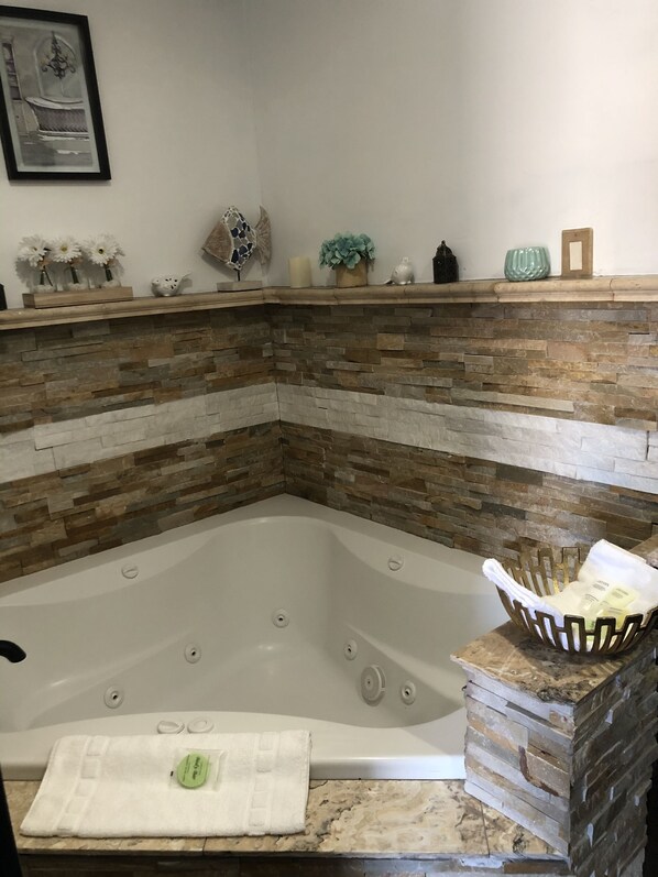A corner bathroom with a stone mosaic wall, a white bathtub, and a shelf with decorative items.