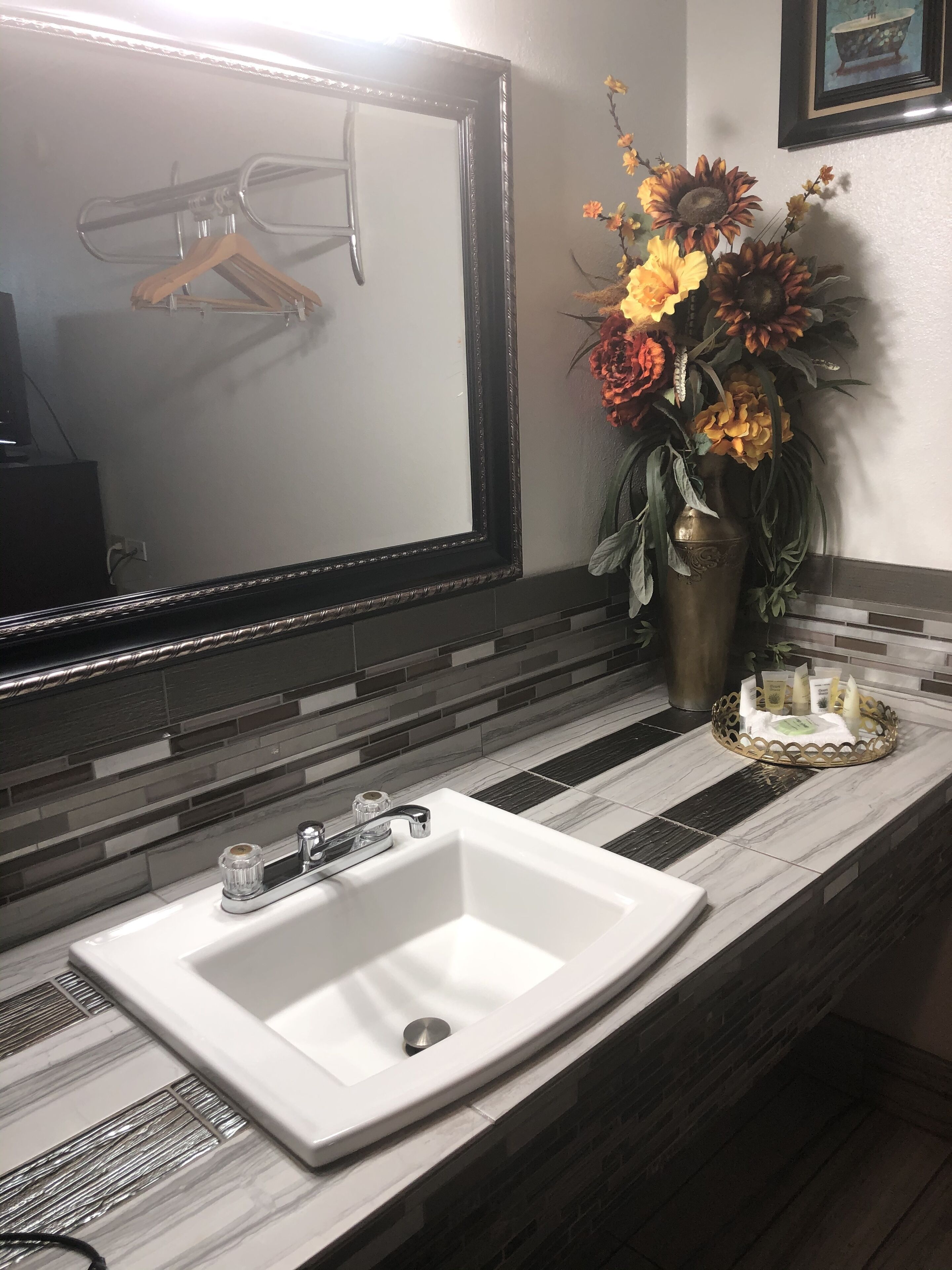 Une salle de bain avec un lavabo blanc, un miroir et un vase de fleurs.