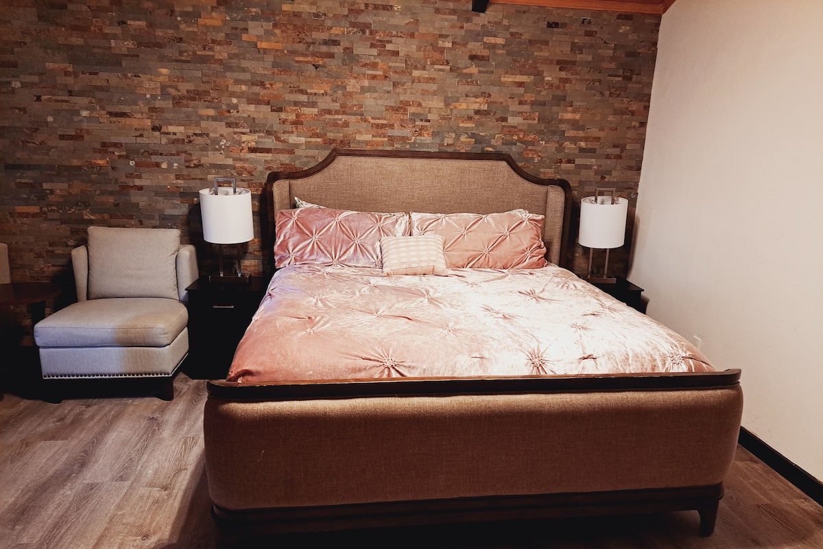 Une chambre avec un grand lit, une chaise, deux tables de chevet et un mur décoré d’un motif en briques.