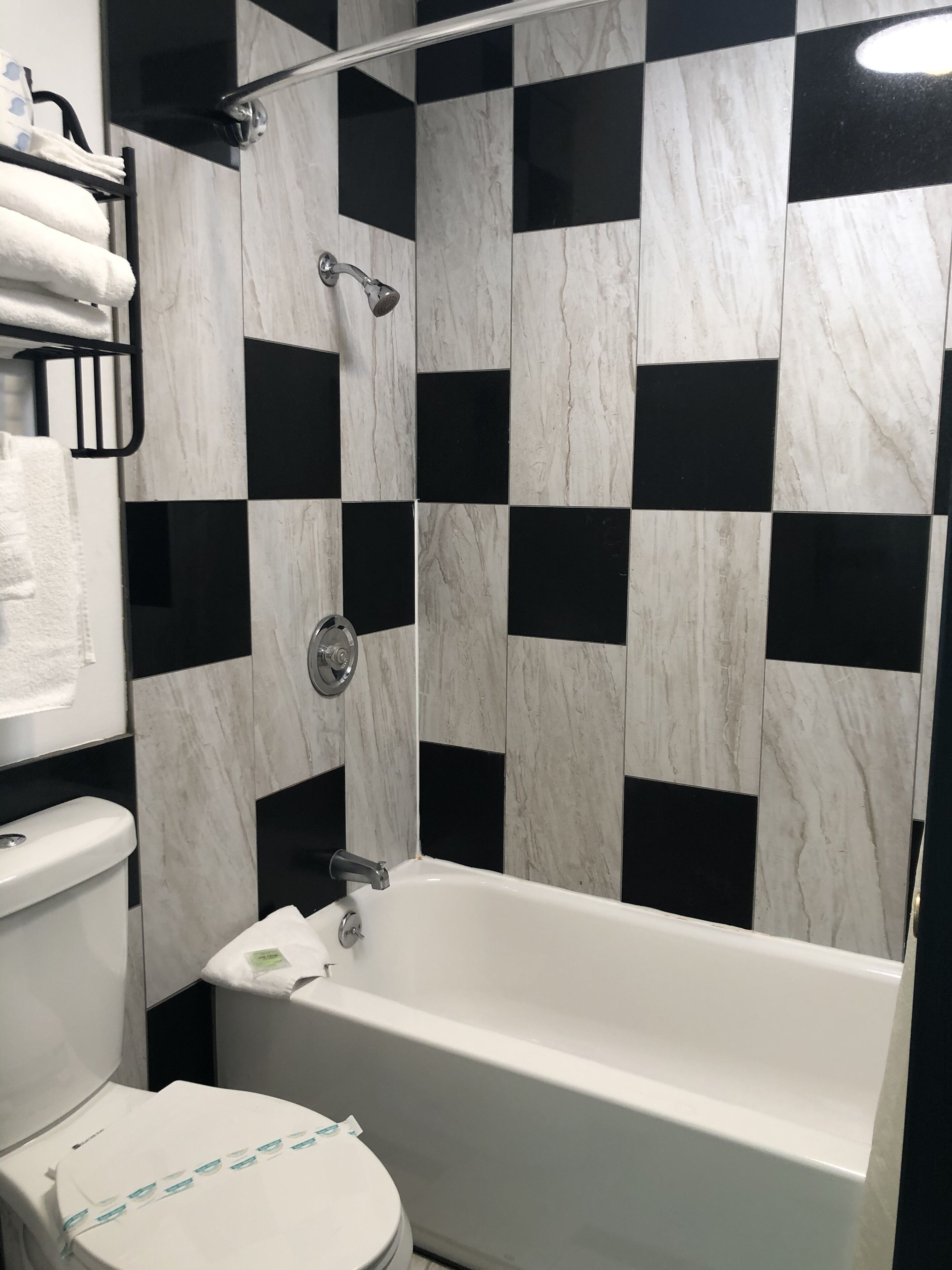 Een badkamer met een witte badkuip, een toilet en een douchegedeelte met zwart-wit schakkend patroon.