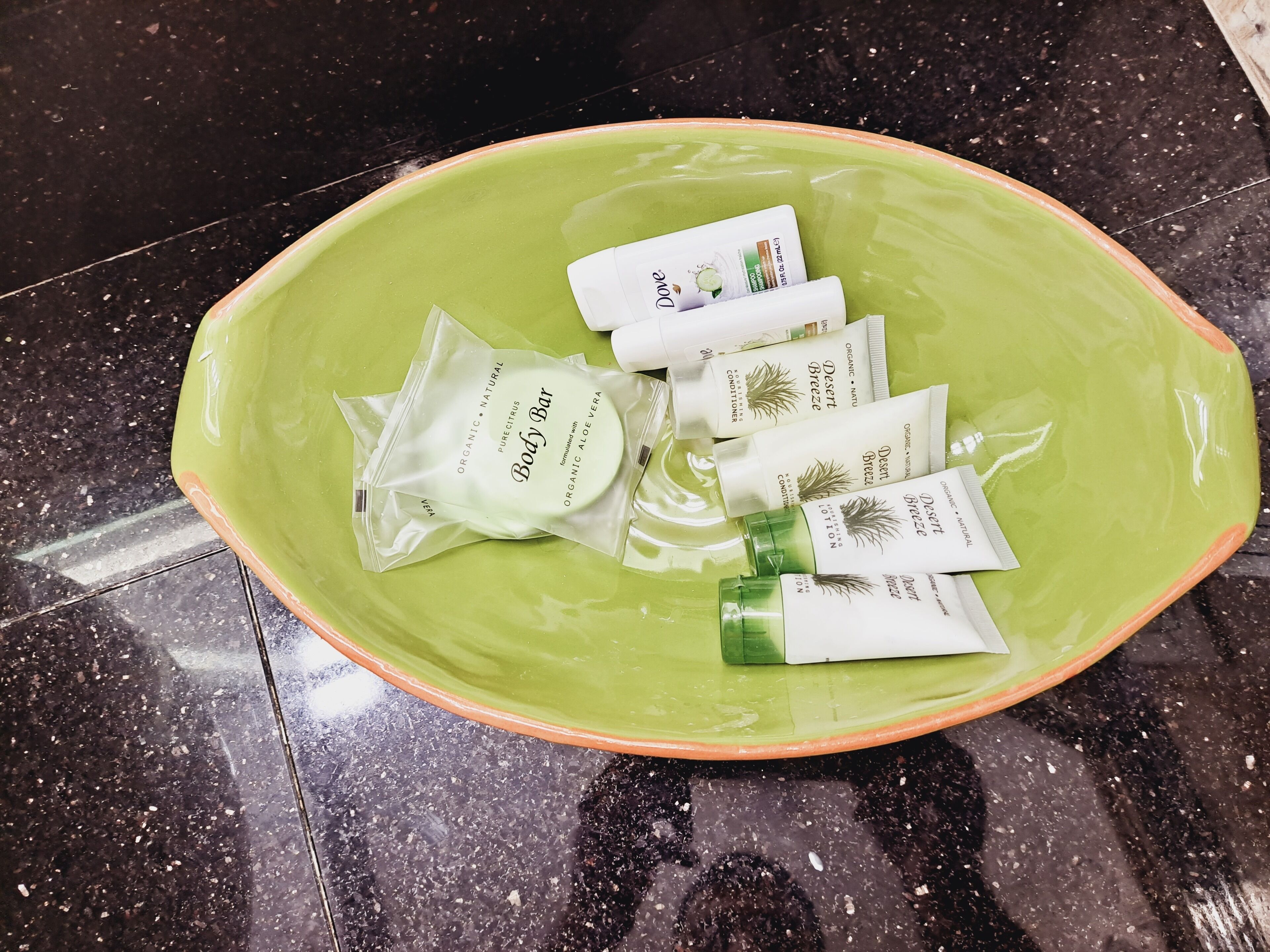 Un bol vert contenant plusieurs petits emballages de savon Dove et de lotion pour le corps.