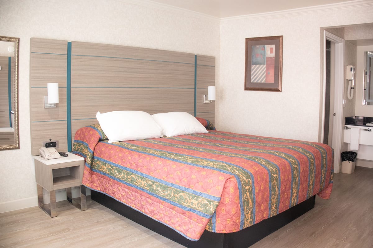 A hotel room with a large bed, bedside tables, a nightstand, a mirror, and a door leading to a bathroom.