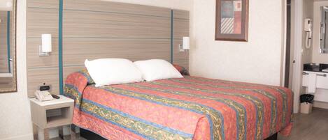 A hotel room with a large bed, bedside tables, a nightstand, a mirror, and a door leading to a bathroom.