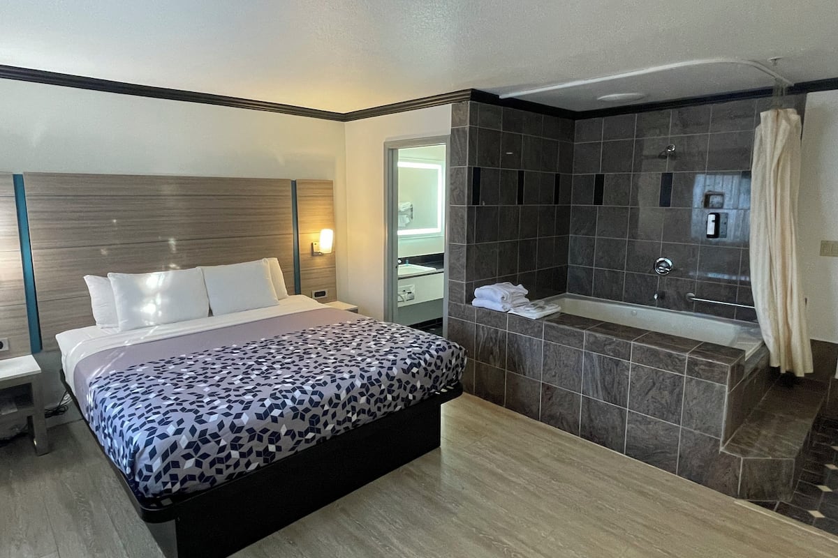 A hotel room with a bed, a bathroom with a bathtub, and a shower.