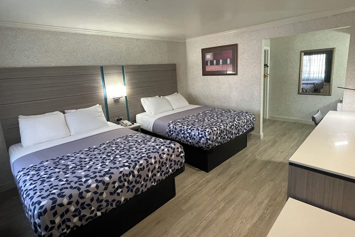 A hotel room with two beds, a desk, and a mirror.