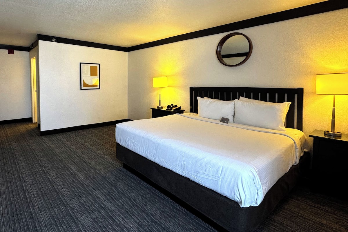 A hotel room with a large bed, two bedside tables with lamps, a round mirror on the wall, and a framed picture on the wall.