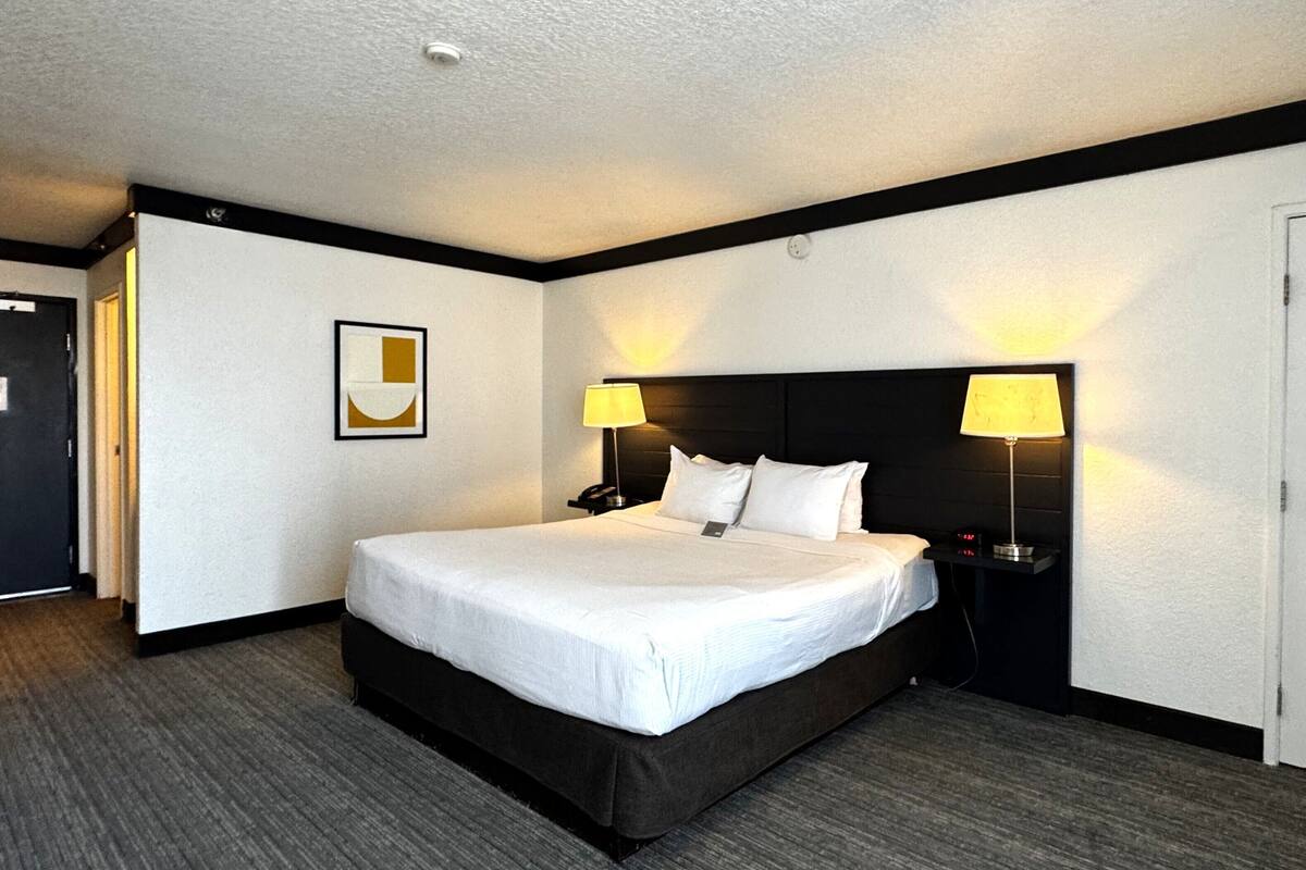 A hotel room with a large bed, two bedside lamps, a nightstand, and a framed picture on the wall.