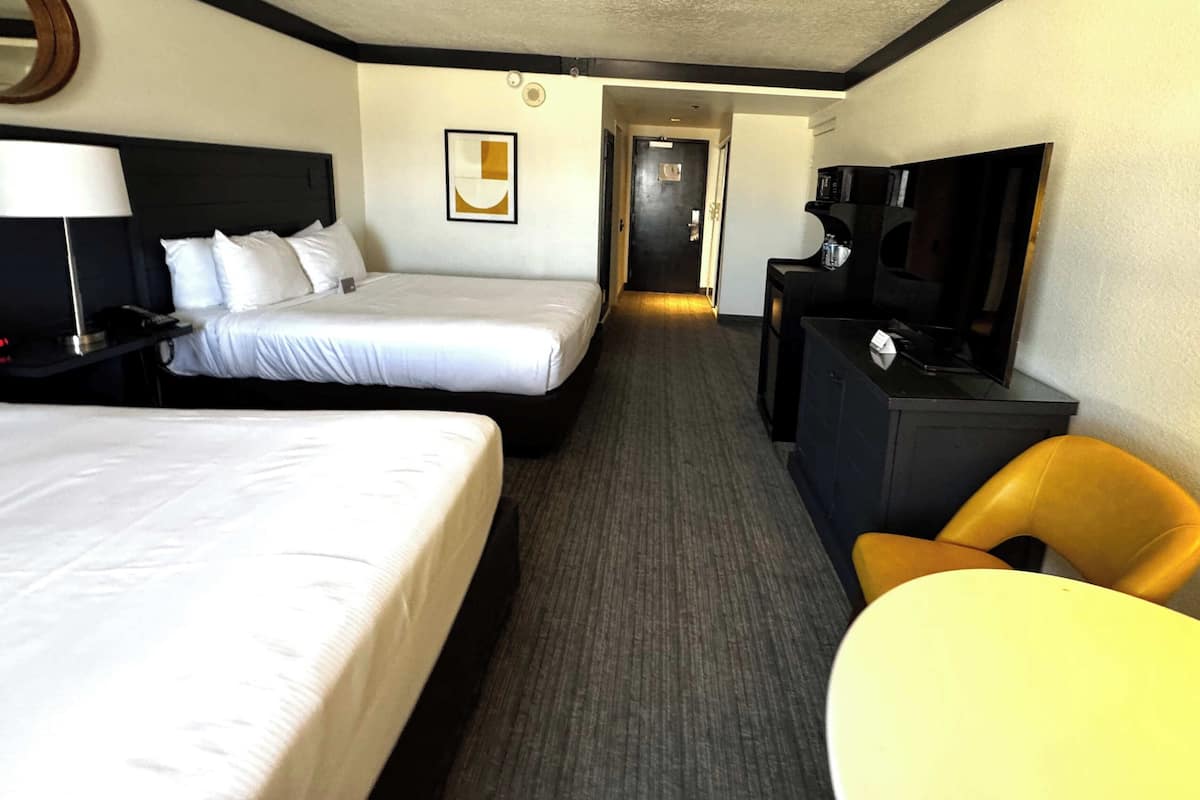 A hotel room with two beds, a desk, a chair, a television, and a framed picture on the wall.
