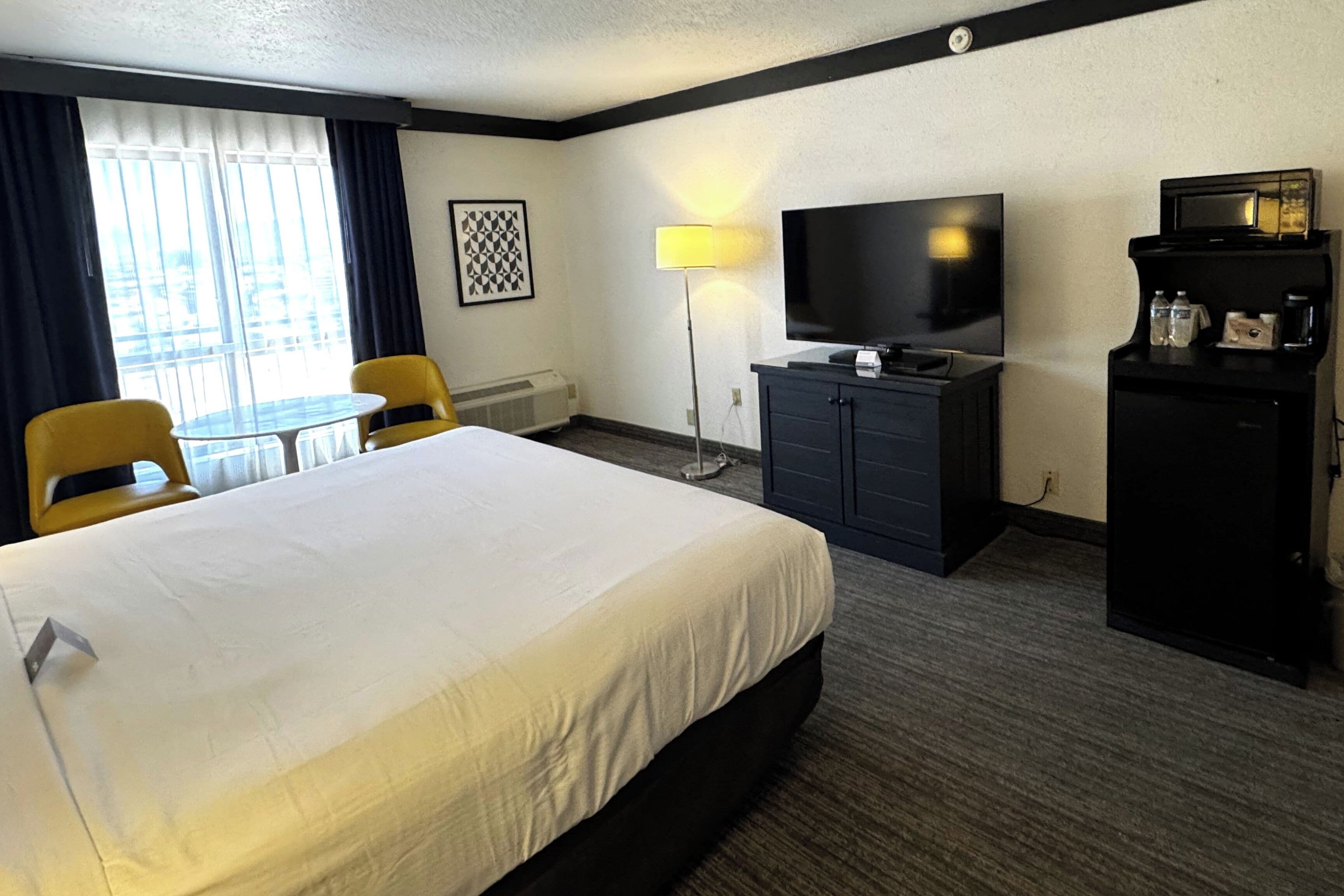 Camera d'albergo con un letto grande, una scrivania, una sedia, una televisione, un minibar e una finestra con tende.