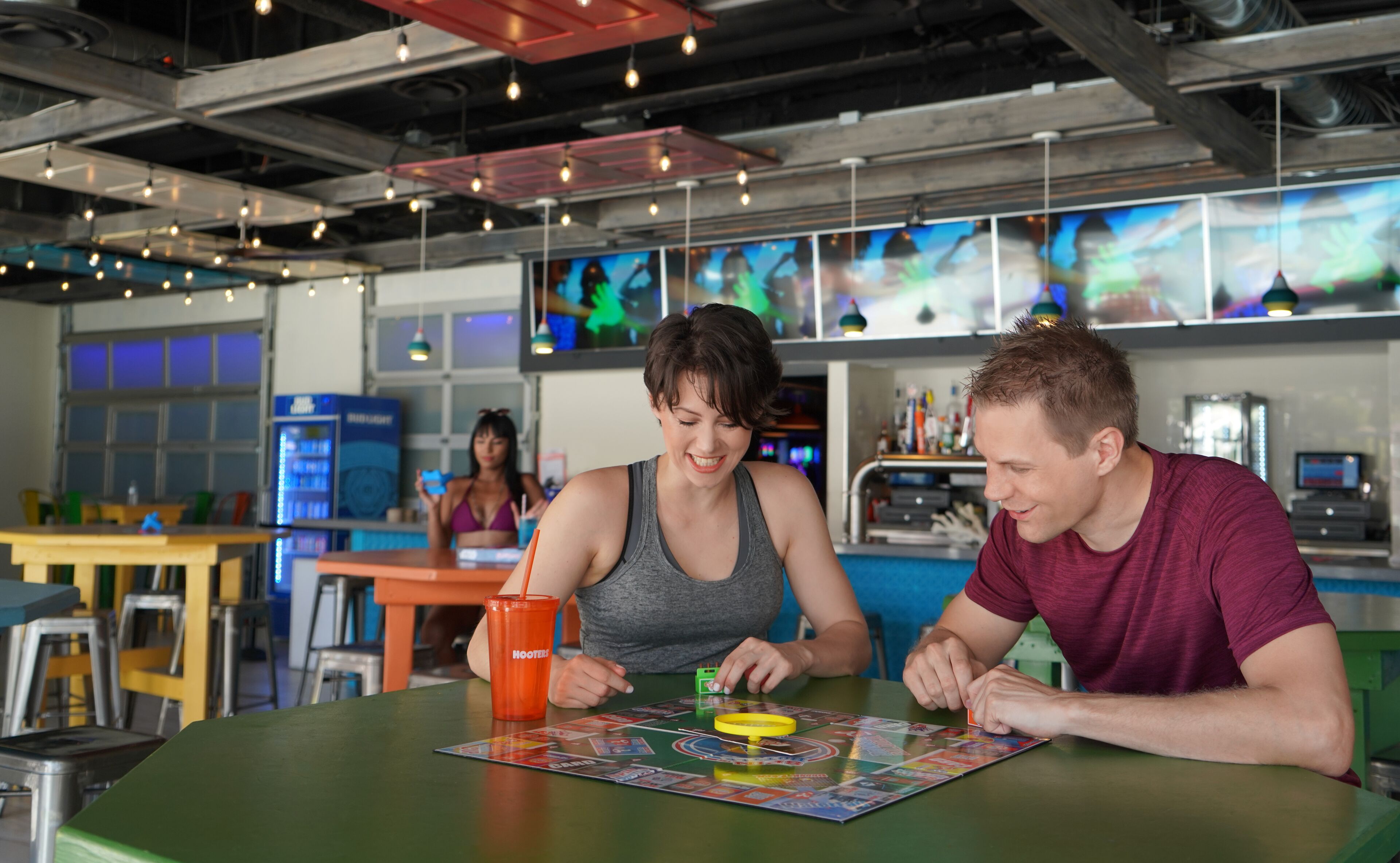 Een groep mensen speelt een bordspel aan een tafel in een ruimtelijke binnenruimte met modern industrieel design.