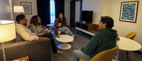 A hotel room with a sofa, two round tables, a TV, and artwork on the walls.
