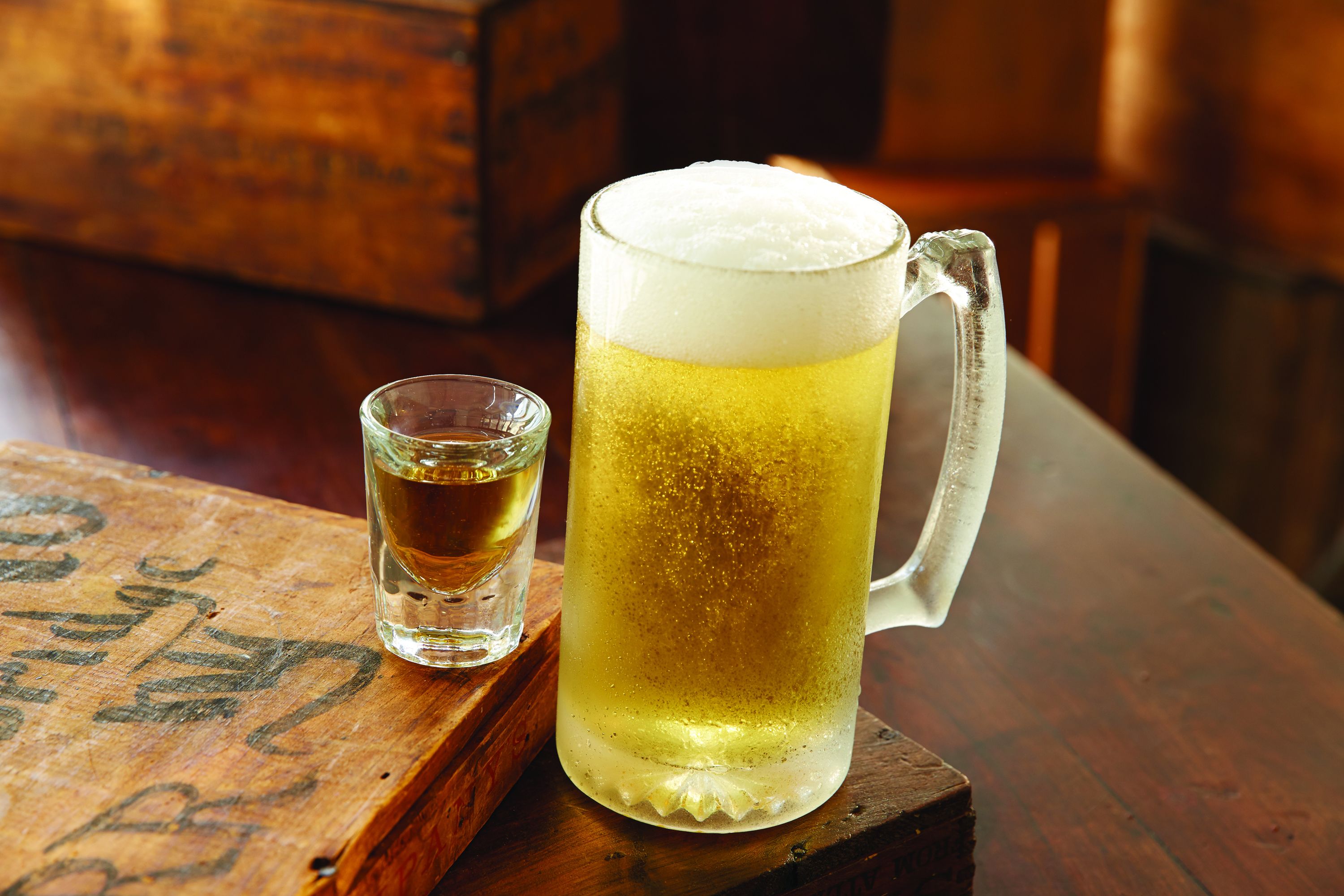 Ein Holztisch mit einem großen Bierglas und einem kleinen Weinglas.