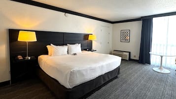 Habitación de hotel con una cama grande, dos lámparas de noche, una mesa redonda y una ventana con cortinas.