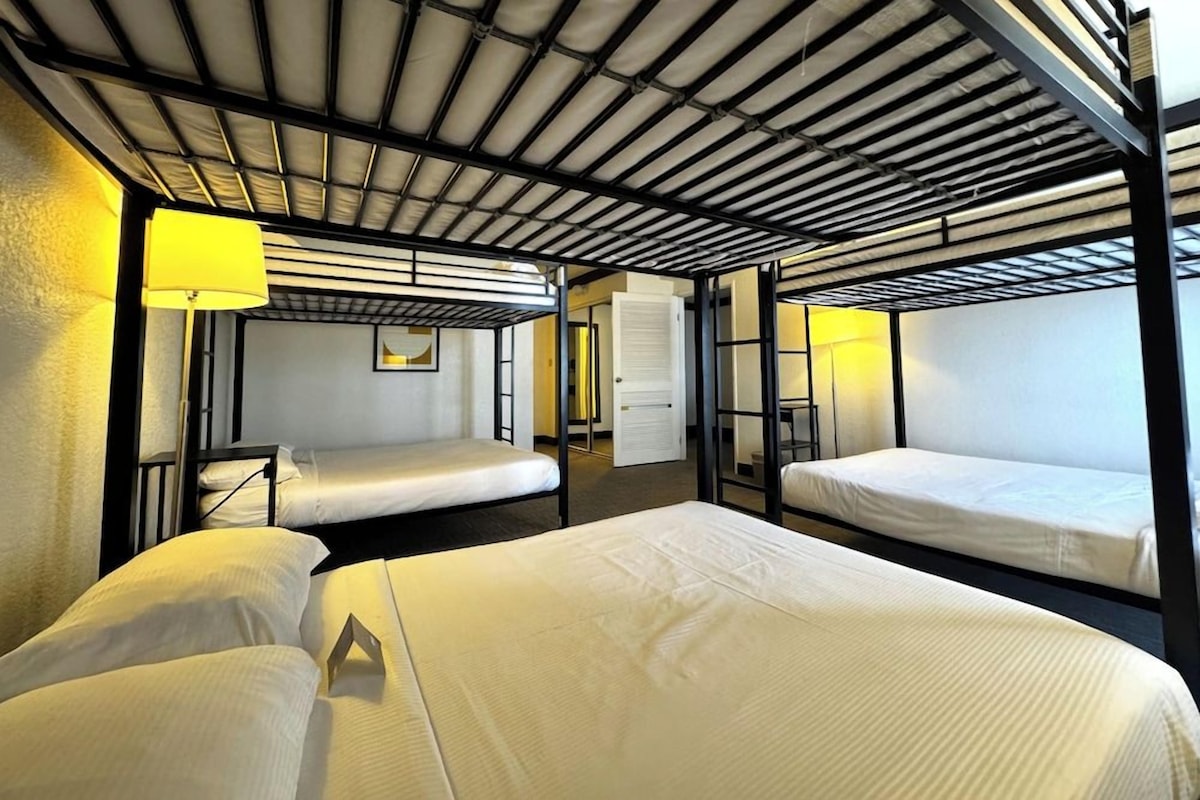 A dormitory-style room with bunk beds, a desk, and a lamp.