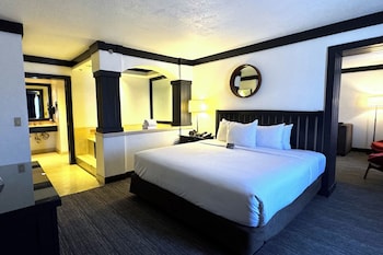 A hotel room with a TV, sofa, two yellow chairs, a small table, and a kitchen area with a microwave. at OYO Hotel and Casino Las Vegas