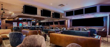 A spacious lounge area with multiple seating options, including sofas and armchairs, and a bar area with a television screen.