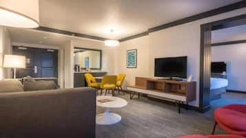 Une chambre d’hôtel avec un canapé, deux fauteuils jaunes, une petite table, un téléviseur et un lit.