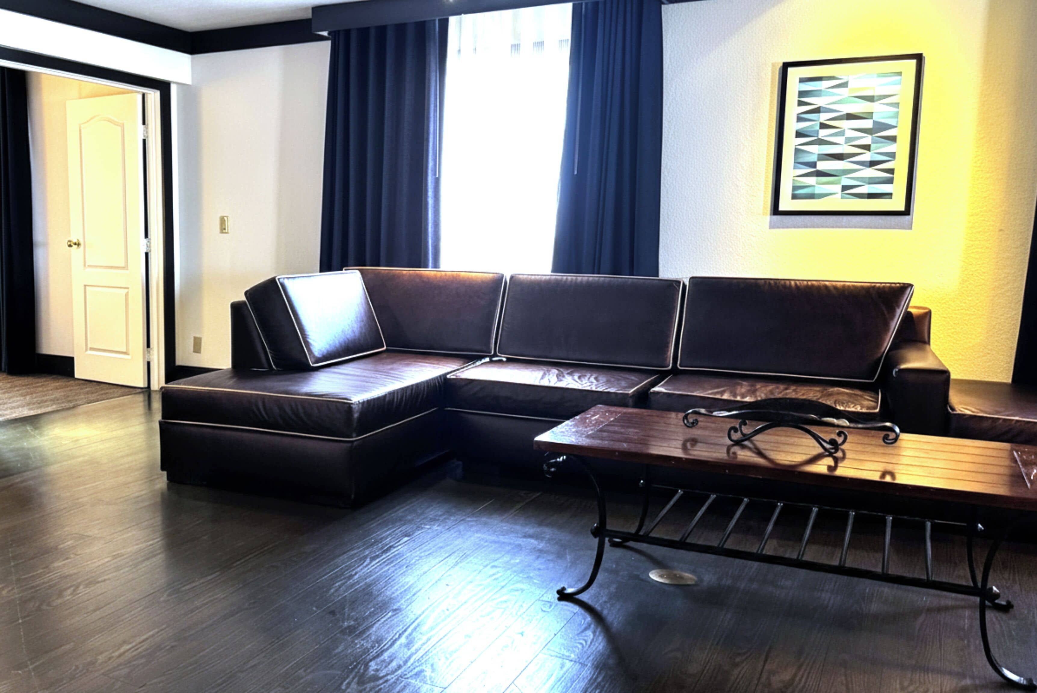 Uma sala de estar moderna com um sofá seccional, uma mesa de centro de madeira e uma janela grande com cortinas.