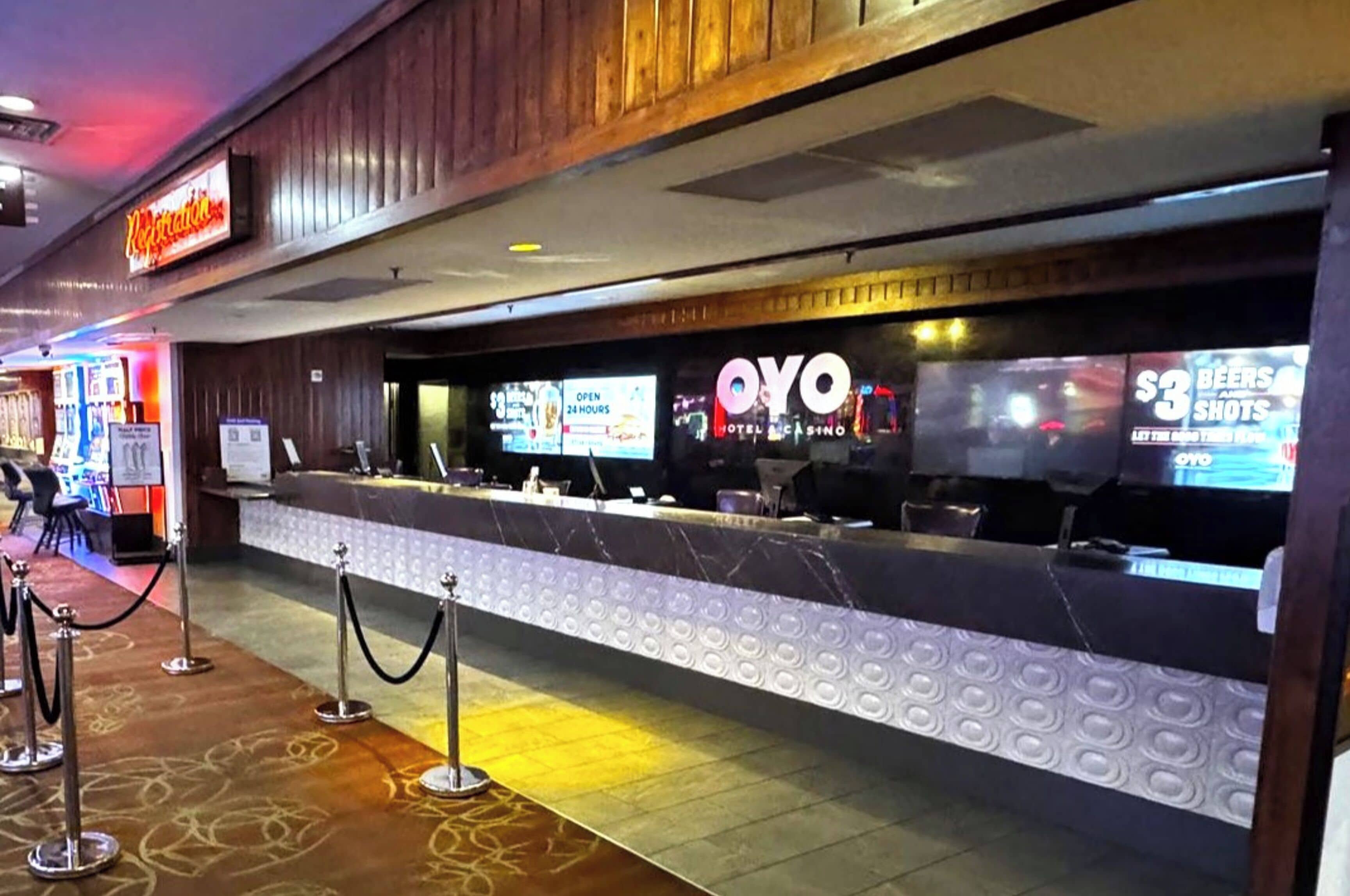 A hotel reception area with a marble counter, a neon sign above, and a digital screen displaying promotions.