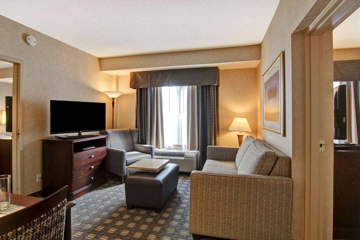 Une chambre d’hôtel équipée d’un téléviseur à écran plat, d’un canapé, d’un fauteuil, d’une petite table et d’une lampe.