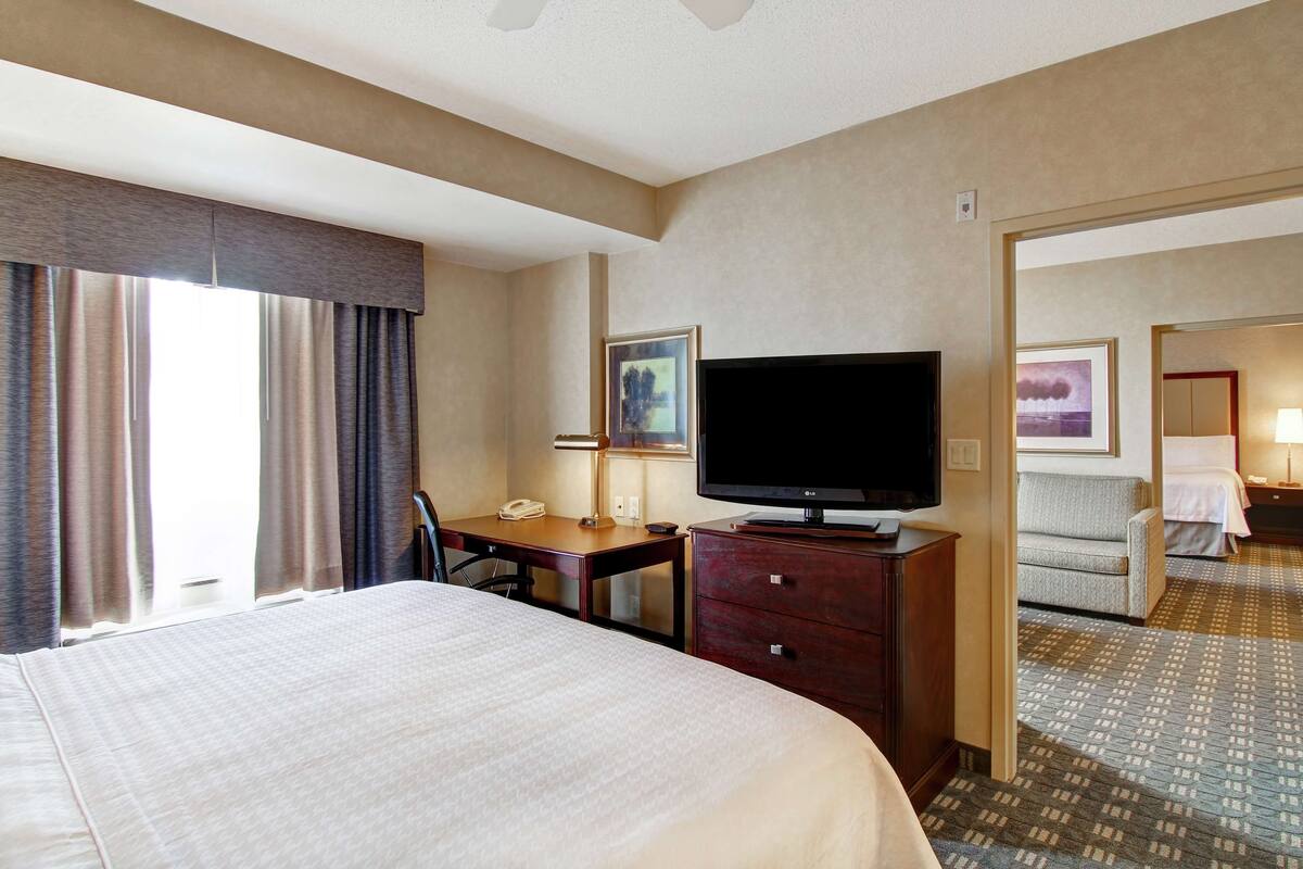Une chambre d’hôtel avec un grand lit, un bureau avec un téléphone, un téléviseur à écran plat et une porte donnant sur une salle de bain.