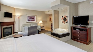 A hotel room with a bed, a sofa, a TV, a fireplace, and a bathtub.