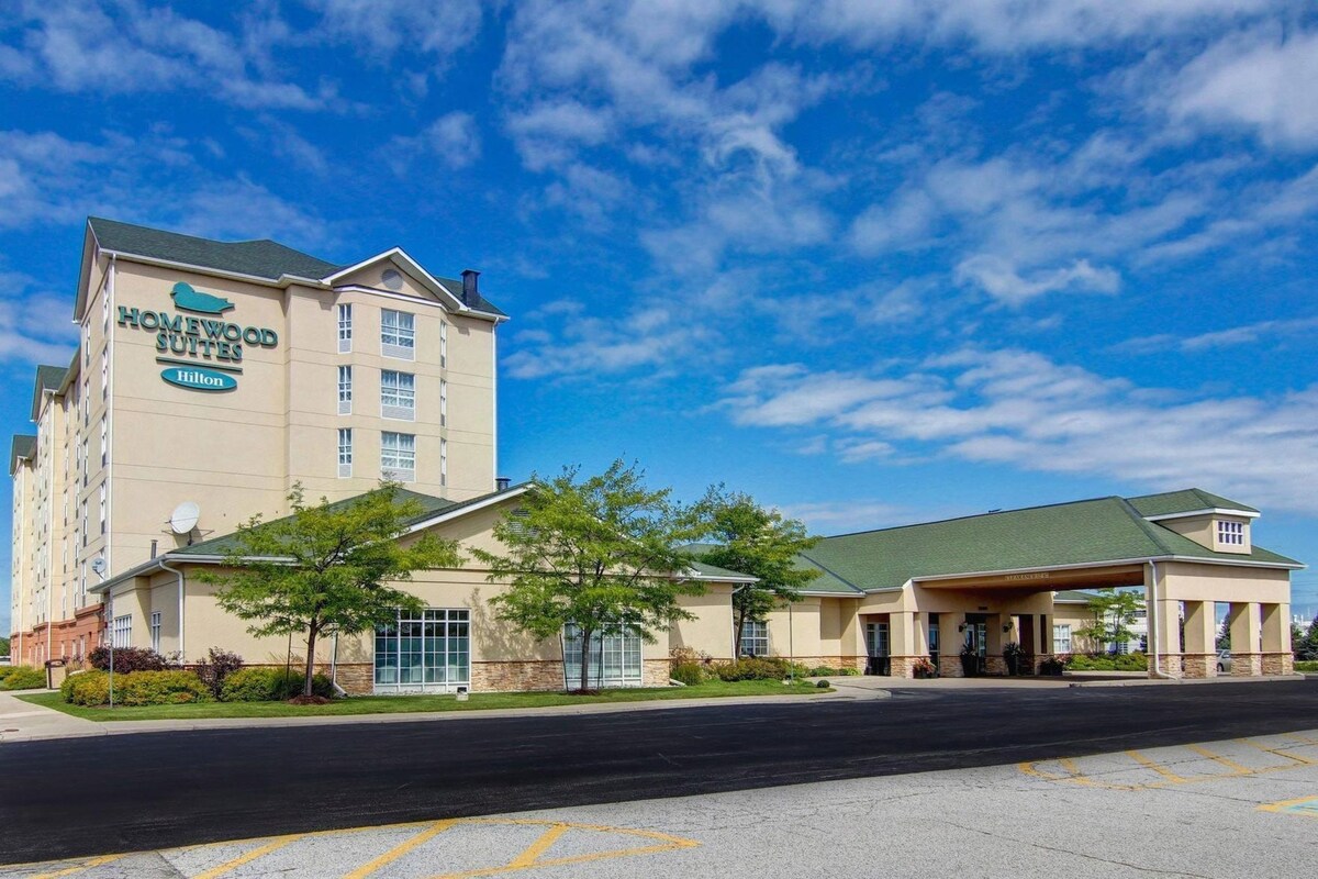 A hotel with a prominent sign for Homewood Suites Hilton, a parking lot, and a building with a green roof.