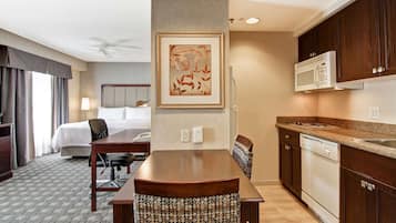 Quarto de hotel com cama, escrivaninha, cadeira, micro-ondas e lava-louças.