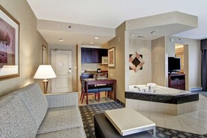 Habitación de hotel con sofá, mesa de comedor, zona de cocina y baño con bañera.