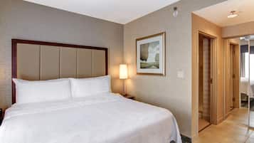 Una habitación de hotel con una cama grande, una lámpara de noche, un cuadro en la pared y una puerta que da a otra habitación.