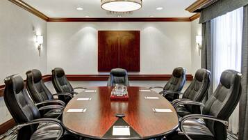 A conference room with a large oval table, eight leather chairs, a red accent table, and a wooden accent wall.