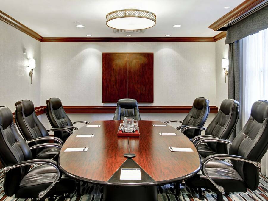 A conference room with a large oval table, eight leather chairs, a red accent table, and a wooden accent wall.