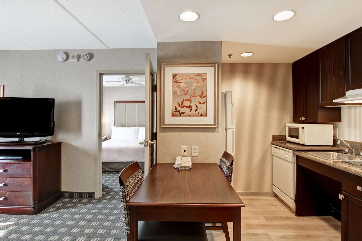 Une chambre d’hôtel équipée d’une table à manger en bois, d’un téléviseur à écran plat, d’un four à micro-ondes et d’un réfrigérateur.