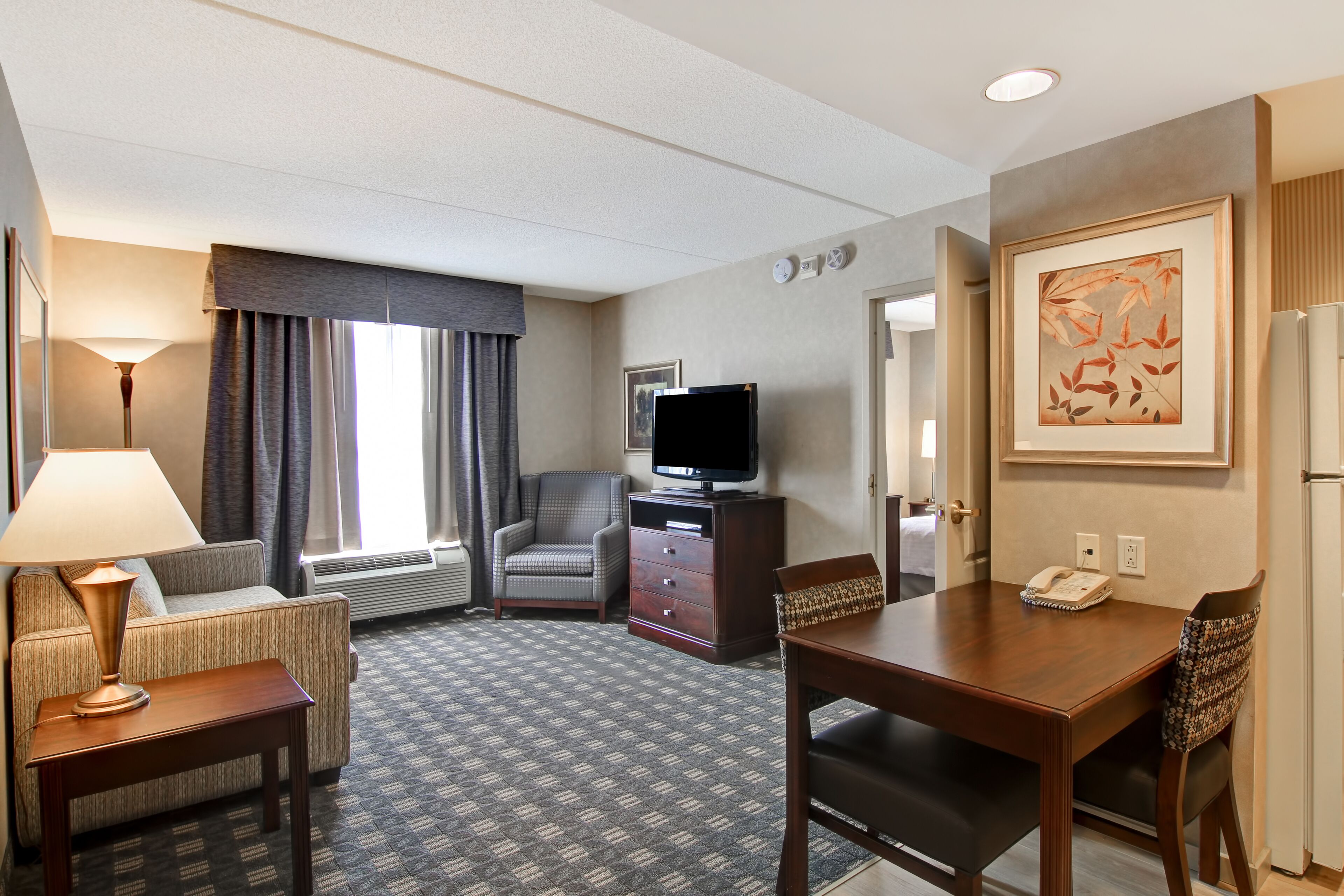 Una habitación de hotel con sofá, sillón, mesa de madera y televisor sobre una cómoda.