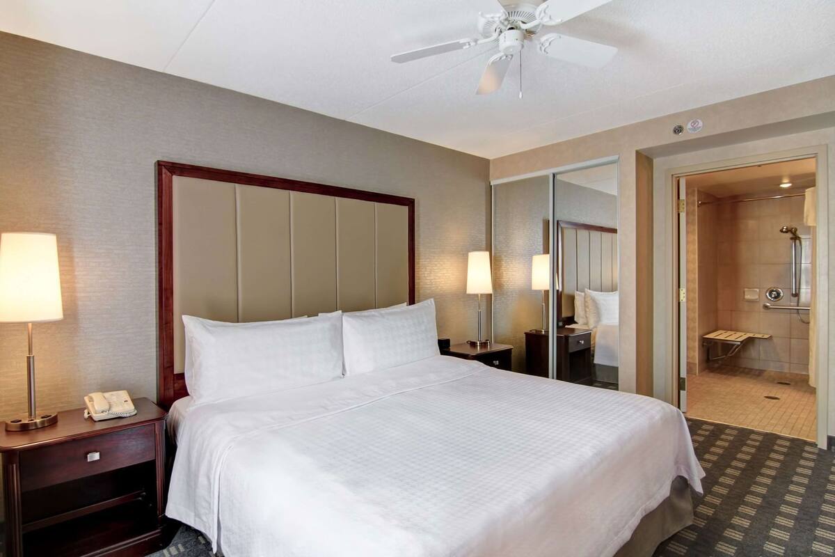 A hotel room with a bed, bedside lamps, a telephone, a mirror, and a shower area.