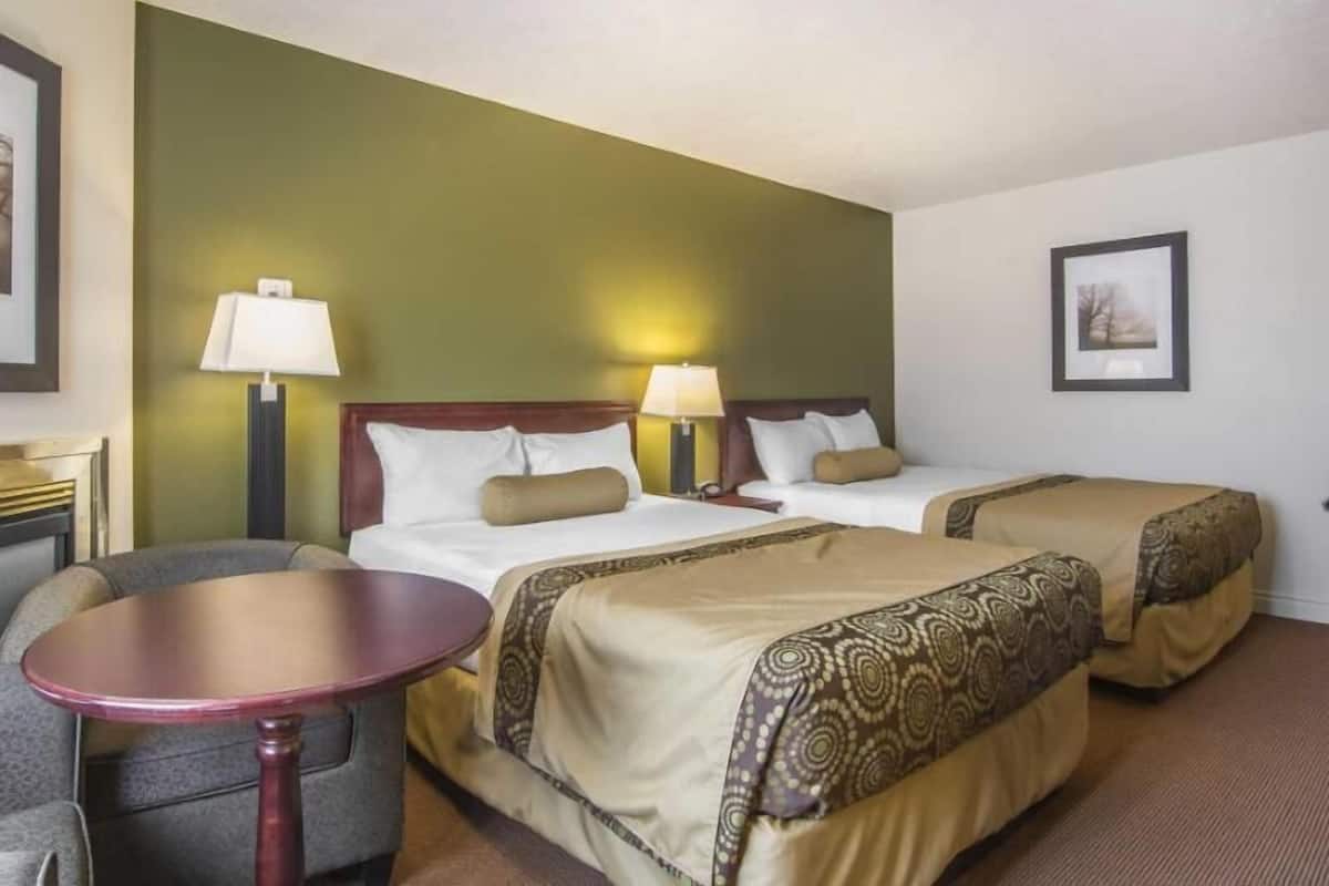 A hotel room with two beds, a small table, and a chair.