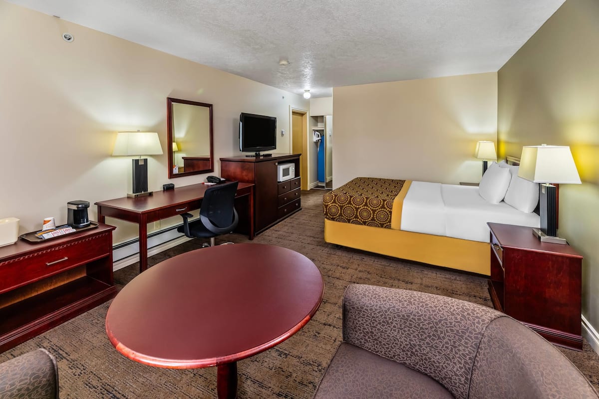 A hotel room with a bed, a desk with a chair, a television, a lamp, and a small table.