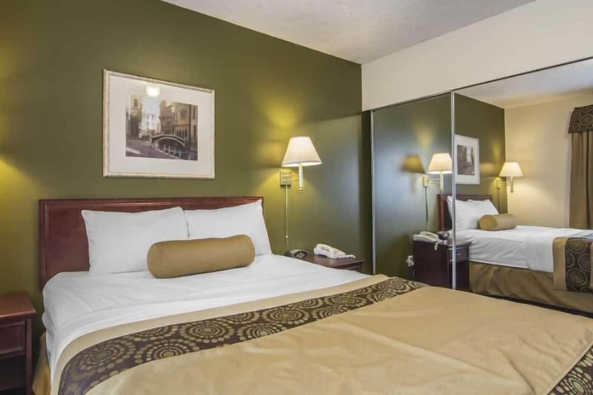 A hotel room with a bed, bedside lamps, a telephone, a framed picture on the wall, and a mirror.
