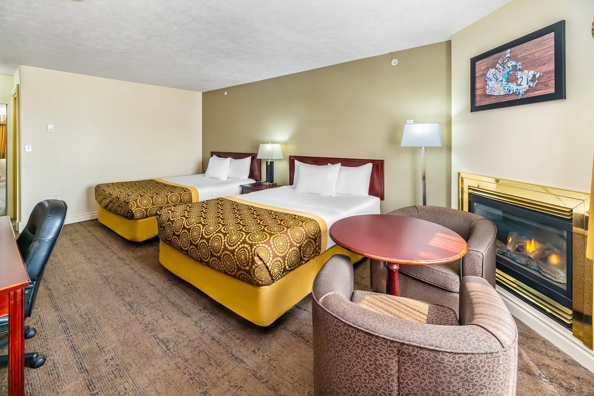 A hotel room with two beds, a sofa, a small table, and a fireplace.
