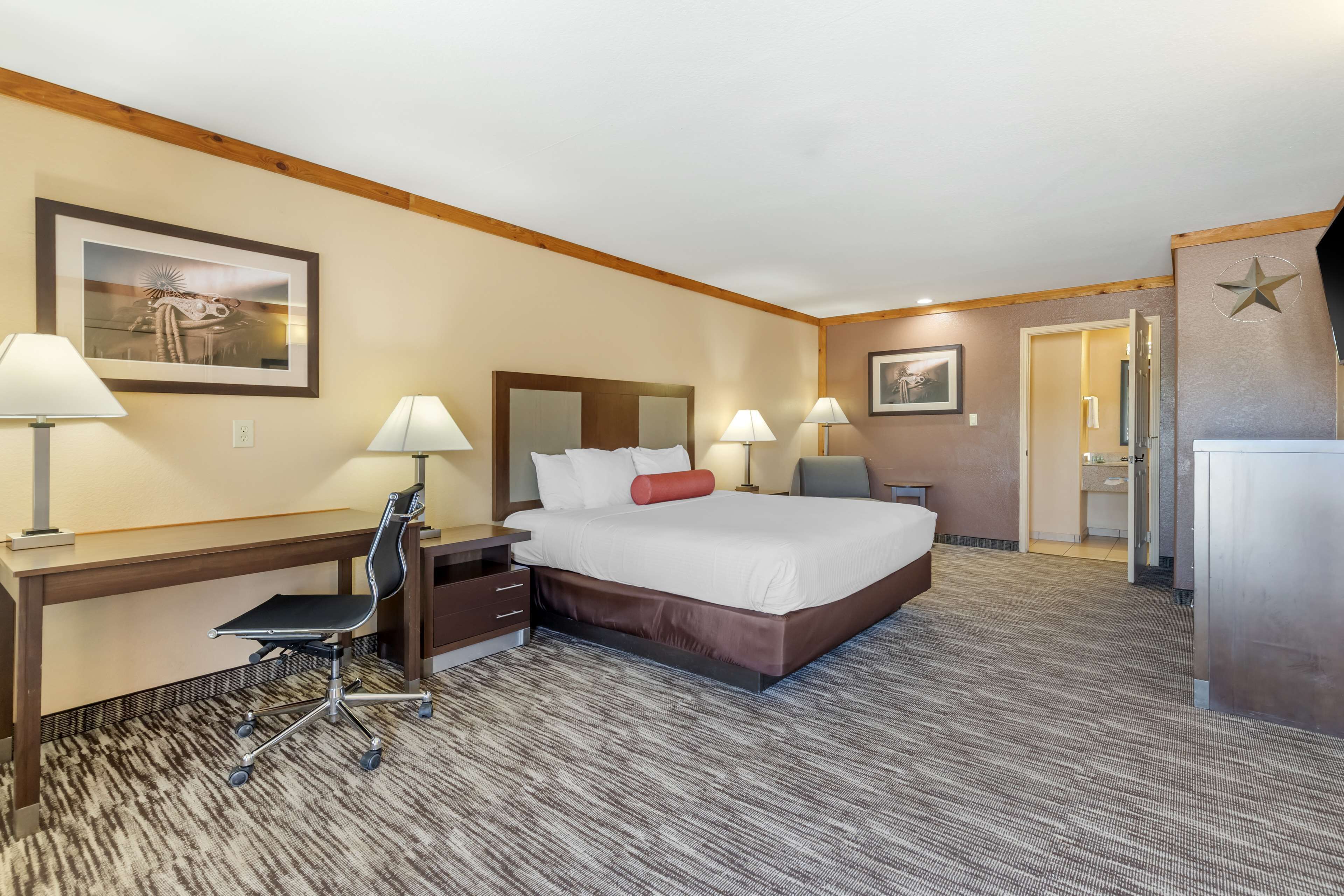 Habitación de hotel con una cama grande, un escritorio con silla, dos lámparas y un cuadro en la pared.