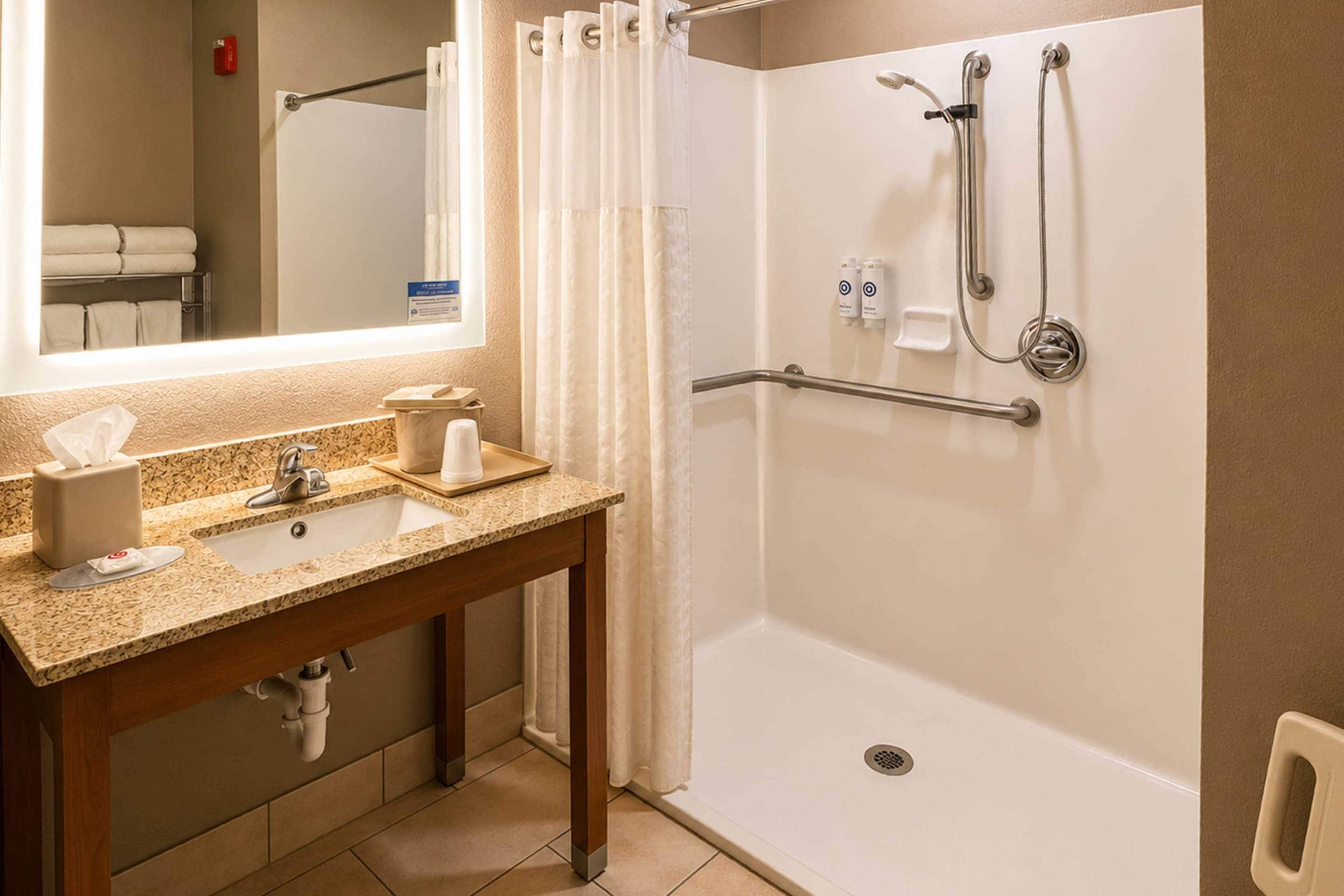 A bathroom with a sink, mirror, shower, and grab bars.