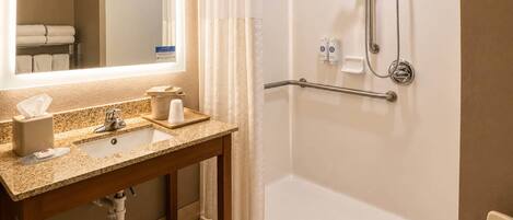 A bathroom with a sink, mirror, shower, and grab bars.