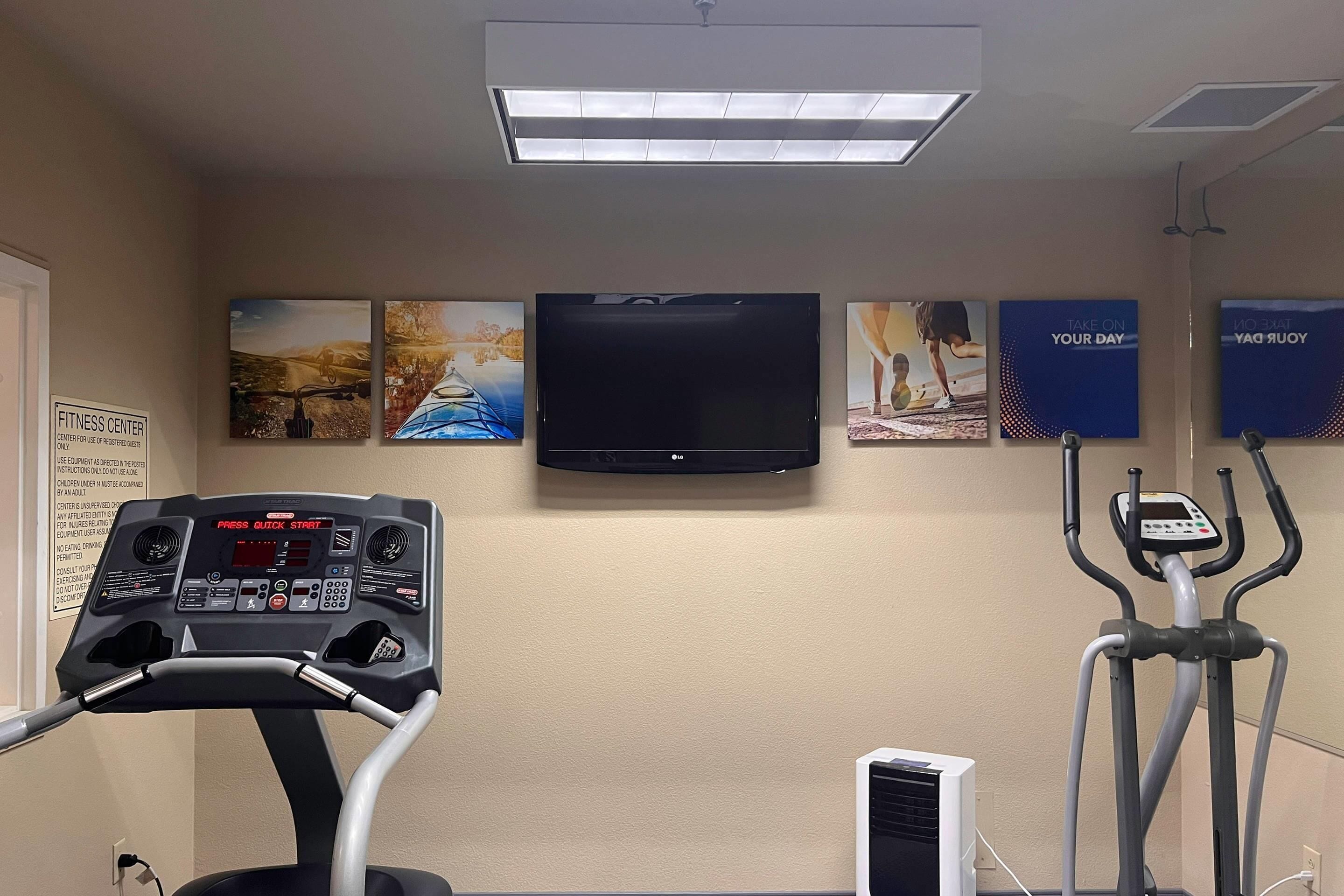A fitness center with exercise equipment, a television, and motivational posters on the wall.