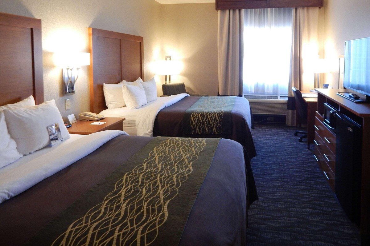 A hotel room with two beds, a desk, a chair, a dresser, and a television.