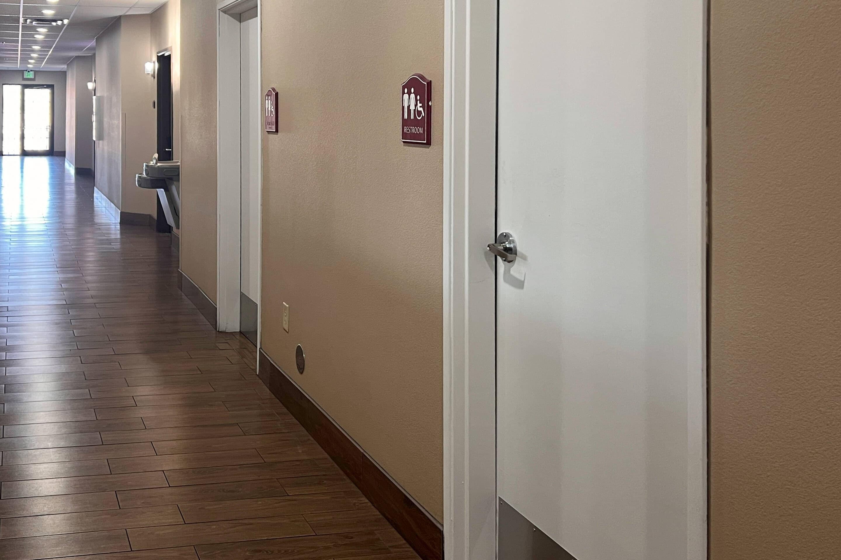 Passadís d'hotel amb senyal de lavabos, un rentamans i una porta.