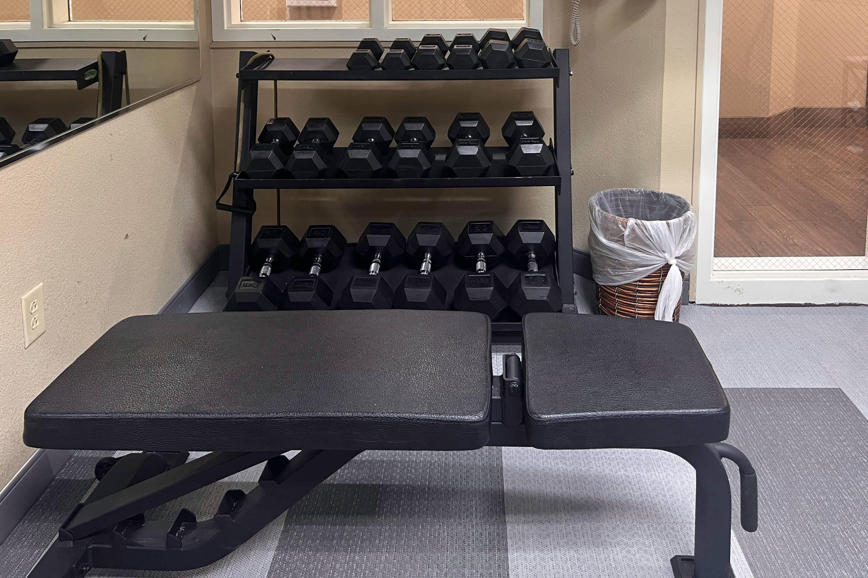 A gym with a bench, dumbbells, and a basket.